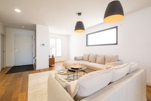 A modern living room with a sofa, coffee table, and pendant lights. - Ovalie - Stunning Family Home with Swimming Pool Just Steps from the Ocean (RIVEDOUX PLAGE)