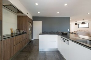 A modern kitchen with a central island, built-in appliances, and a dining area with a sofa. - Ovalie - Stunning Family Home with Swimming Pool Just Steps from the Ocean (RIVEDOUX PLAGE)