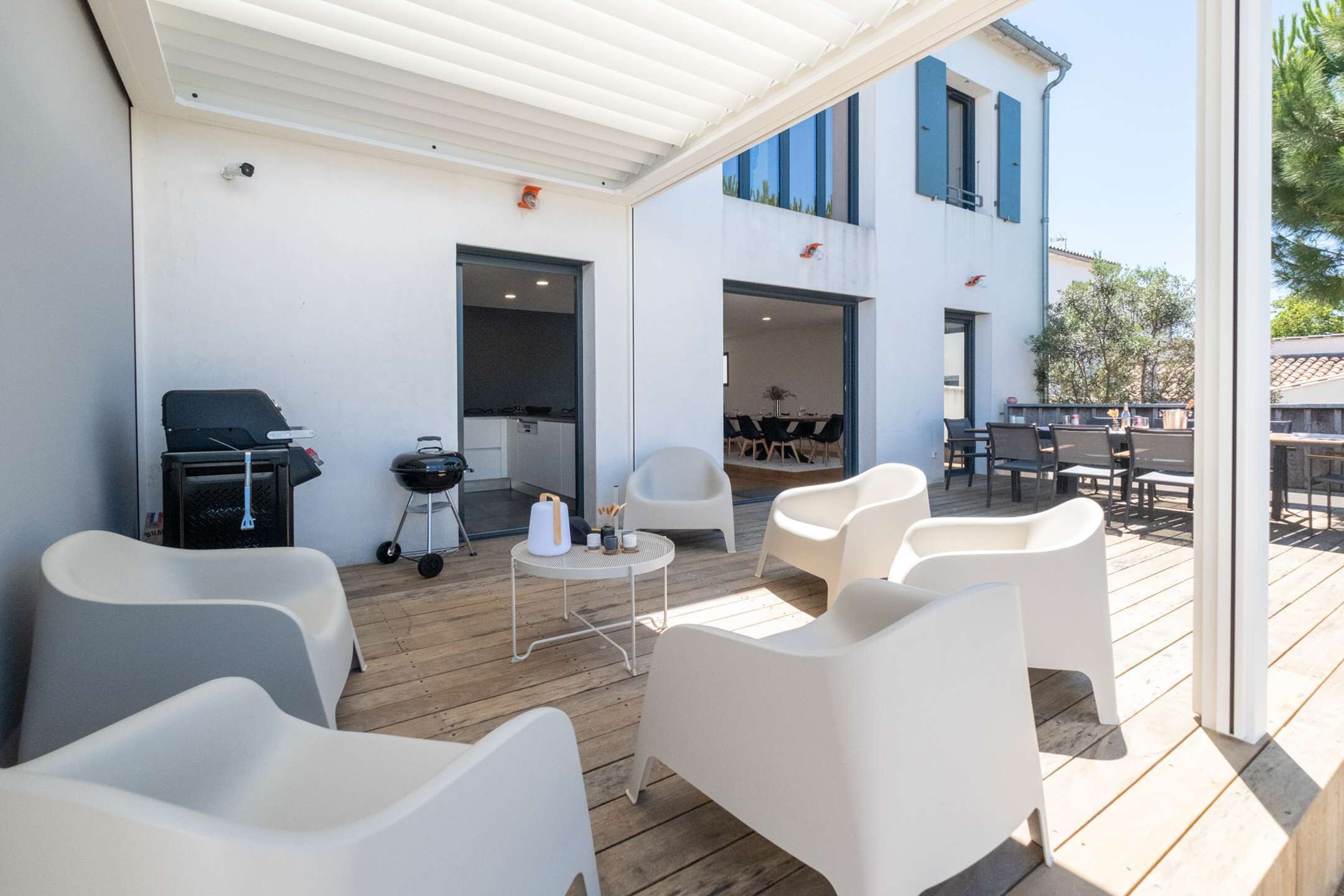 A covered outdoor seating area with white chairs, a grill, and a small table.