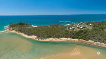 An aerial view of Peter's Cottage, featuring a coastal landscape with a sandy beach and dense greenery.