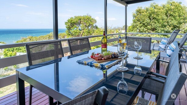 A table set for dining with a view of the ocean, outdoor seating, and a bottle of wine. - PETER'S COTTAGE - A COASTAL GEM IN HISTORIC 1770 (SEVENTEEN SEVENTY)