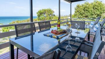A table set for dining with a view of the ocean, outdoor seating, and a bottle of wine.