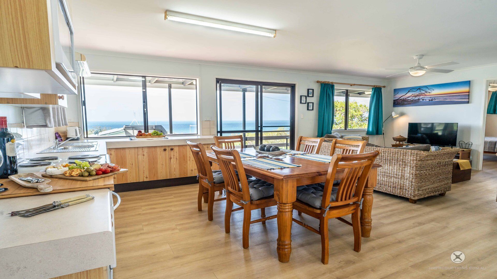Un grand espace à manger avec une table et des chaises en bois, une cuisine avec vue et un salon équipé d’un téléviseur et agrémenté d’un tableau.