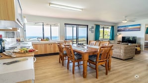 A spacious dining area with a wooden table and chairs, a kitchen with a view, and a living area with a TV and a painting. - PETER'S COTTAGE - A COASTAL GEM IN HISTORIC 1770 (SEVENTEEN SEVENTY)