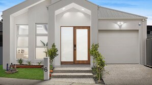 Een modern huis met twee verdiepingen, een garage, een voordeur met geëtste glaspanelen en een kleine tuin met potplanten.