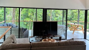 Un saló modern amb un televisor gran, sostre de fusta i grans finestres que donen a l'exterior.