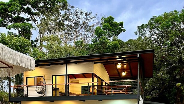 Una casa moderna de dos pisos amb piscina, mobiliari exterior i vegetació abundant.