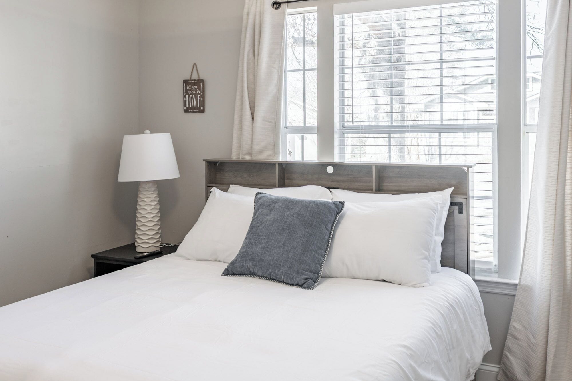 A bedroom with a bed, a nightstand, a lamp, and a window with blinds.