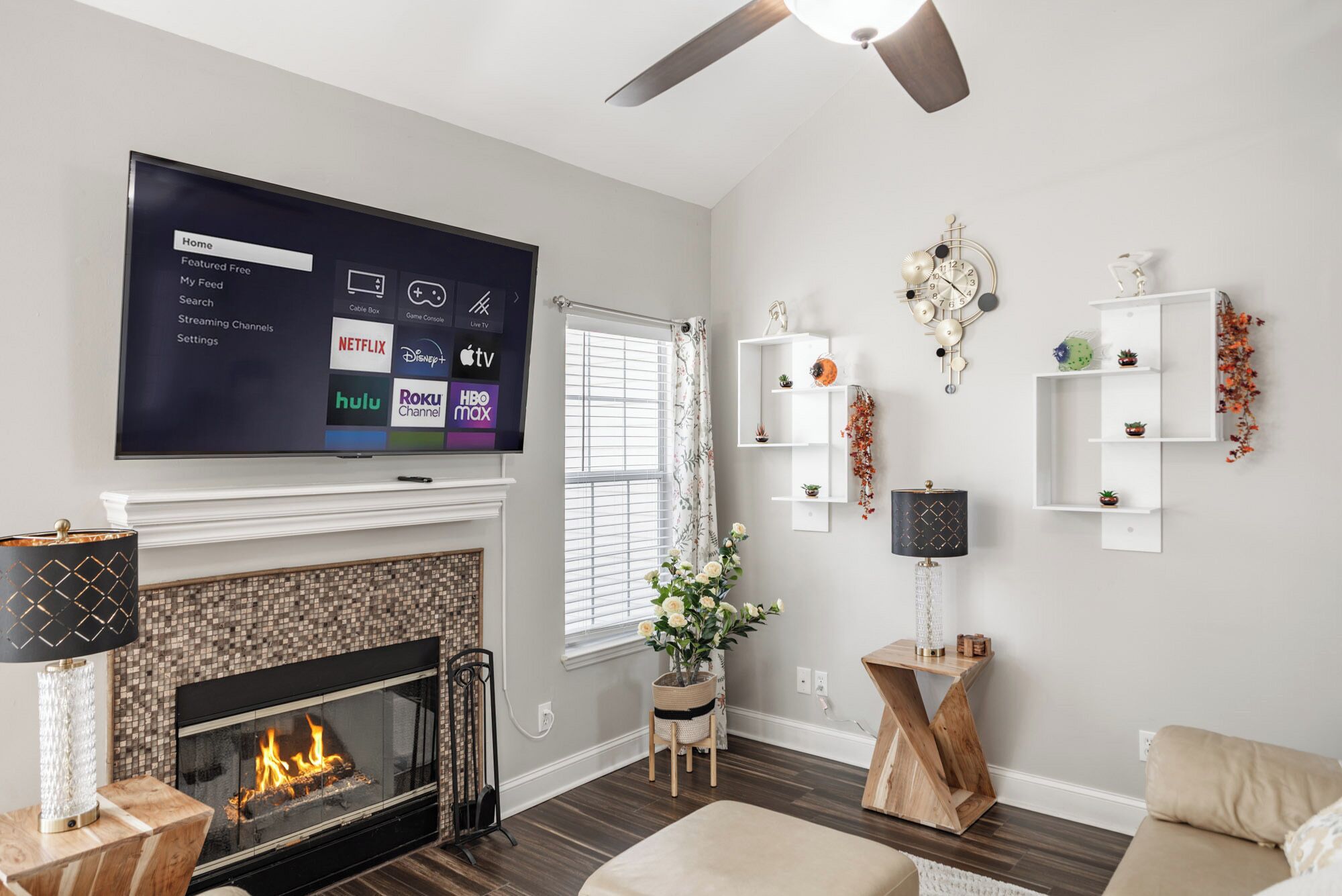 A modern living room with a fireplace, a mounted flat-screen TV displaying streaming services, and a ceiling fan.