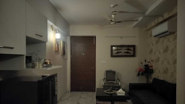 A living room with a sofa, a coffee table, a TV, and a ceiling fan. - Luxury 1BHK Retreat in Sector 106 - Pool, Gym & Premium Comfort (Gurugram)