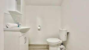 A small, white bathroom with a toilet, sink, and cabinet. - Station-side Top-floor Studio (London)