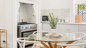Et moderne køkken med hvide skabe, en gasblus, en mikrobølgeovn og et spisebord i glas med stole.