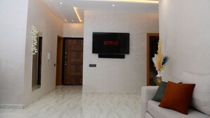 A modern living room with a flat-screen TV mounted on the wall, a sofa with cushions, and a decorative vase with dried flowers.