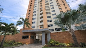 Un edificio residencial de gran altura con fachada de ladrillo, varios balcones y un acceso con portón.
