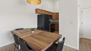 Une cuisine moderne avec des meubles en bois, un réfrigérateur noir et un coin repas comprenant une table en bois et des chaises noires.