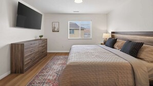 Une chambre à coucher comprenant un lit, une commode, un téléviseur à écran plat, une fenêtre avec des stores et un luminaire au plafond.