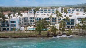A multi-story hotel with a pool, surrounded by palm trees and overlooking a beach. - Imperial Suite 2 Bedroom Ocean View With Kitchen (Sosúa)