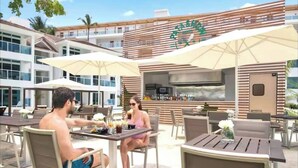 An outdoor dining area with tables and chairs, umbrellas, and a bar area with a wooden facade. - Imperial Suite 2 Bedroom Ocean View With Kitchen (Sosúa)