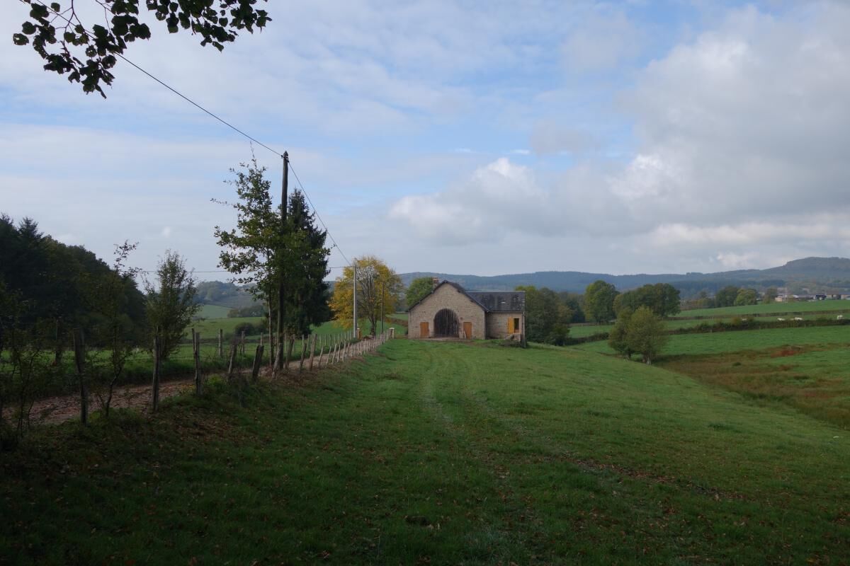 A rural landscape with a stone building, a fenced field, and distant hills.