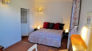 Un dormitorio con una cama, dos lámparas de noche, una silla, una puerta y una ventana con cortinas.