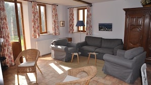 Una sala de estar con un sofá gris, sillones de mimbre, una mesita y un radiador.