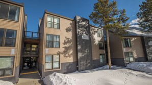 Un edificio de varios pisos con el suelo cubierto de nieve, un letrero que indica que no se utiliza sal en las unidades nuevas, y un árbol en primer plano.