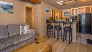 Una sala de estar acogedora con un sofá, una mesa de centro y una cocina equipada con refrigerador, microondas y taburetes de bar.