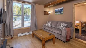 Una sala de estar acogedora con una mesa de centro de madera, sofá gris y una ventana con cortinas.