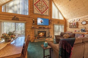 Ein rustikales Blockhaus-Interieur mit Kamin, Fernseher, Esstisch mit Stühlen und einer Couch.