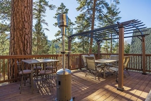 En træterrasse med udendørs møbler, en pergola og et stort træ.