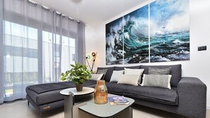 A modern living room with a grey sofa, a small coffee table, a potted plant, and a large ocean wave painting on the wall. - House 2417/192118 (Istria - Medulin), 250m from the beach (Medulin)