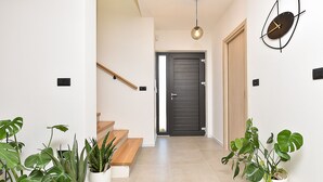 A modern hallway with a wooden staircase, potted plants, a wall-mounted clock, and a door leading to another room. - House 2417/192118 (Istria - Medulin), 250m from the beach (Medulin)