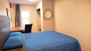 A bedroom with a bed, a chair, a desk, and a mirror on the wall. - Marda Loop Blue Bungalow (Calgary)