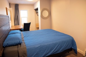 A bedroom with a bed, a chair, a desk, and a mirror on the wall. - Marda Loop Blue Bungalow (Calgary)