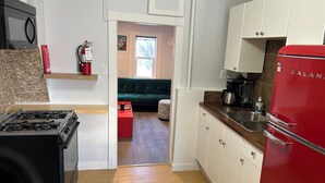 A compact kitchen with a gas stove, a red refrigerator, and a coffee maker. There is a wooden countertop and a green sofa in the adjacent living area. - Marda Loop Blue Bungalow (Calgary)