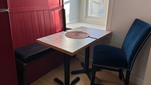 A small, cozy room with a red partition, a wooden table, a blue chair, and a window with a view of the outside. - Marda Loop Blue Bungalow (Calgary)