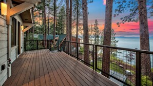 Eine Holzterrasse mit Geländer, die auf einen Wald und ein Gewässer blickt.
