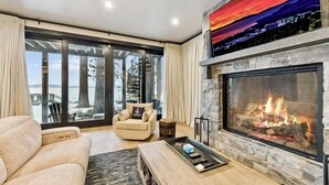 Ein modernes Wohnzimmer mit Kamin, einer Couch, einem Couchtisch und Blick ins Freie.