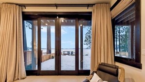 Ein Zimmer mit einer Schiebeglastür, die auf einen Balkon mit Blick auf einen Strand und eine Holzterrasse führt.