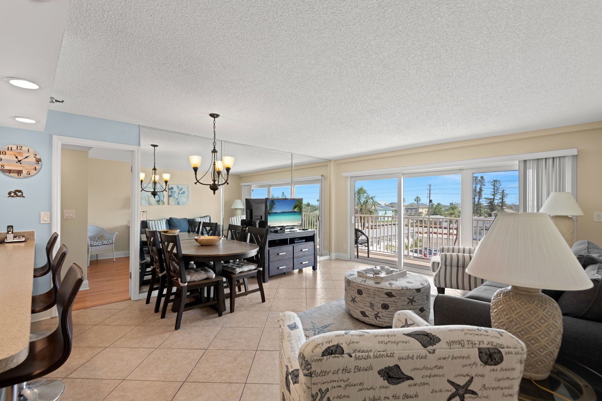 A spacious living area with a dining table, chairs, a sofa, and a balcony with a view.
