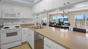 Una cucina moderna con mobili bianchi, forno a microonde integrato, piano cottura e lavastoviglie. È presente una grande isola con lavello e un'area pranzo con sedie e tavolo.