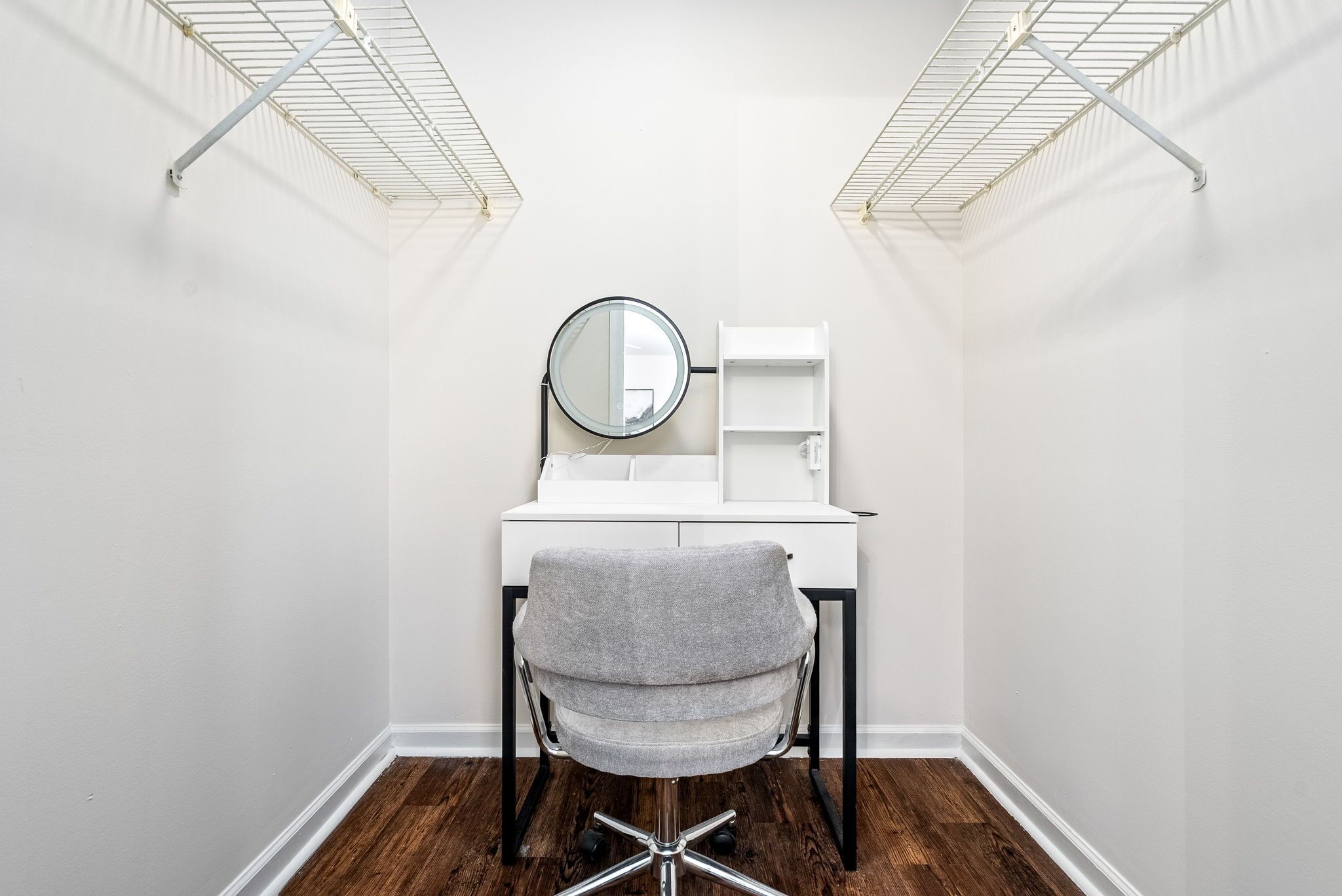 Une petite pièce aux murs blancs, avec un bureau, une chaise et un miroir.
