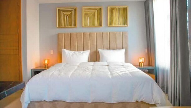Quarto de hotel com uma cama, duas mesas de cabeceira e três luminárias fixadas na parede.