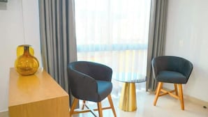Quarto moderno com escrivaninha de madeira, duas cadeiras escuras, uma mesa redonda pequena e um vaso amarelo.