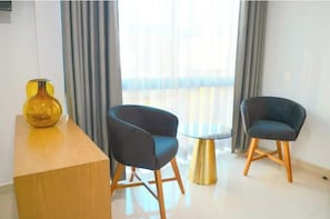 A modern room with a wooden desk, two dark chairs, a small round table, and a yellow vase.