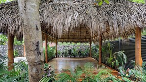 A covered outdoor area with a wooden deck, surrounded by tropical plants and a stone wall. - Villa Ave del Paraiso, 7-bedroom Bed & Breakfast Villa in Playa Avellanas (Playa Avellanas)