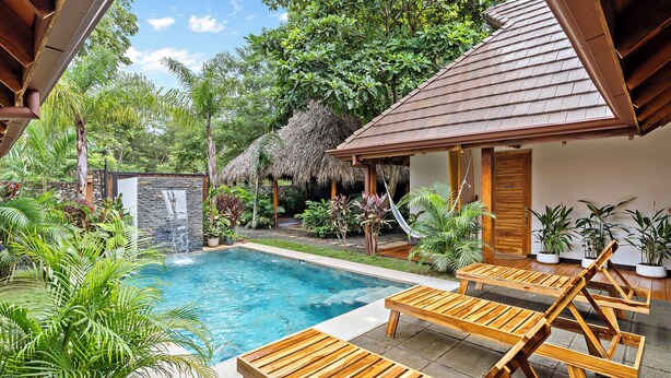 A pool area with wooden loungers, a stone wall, and lush greenery. - Villa Ave del Paraiso, 7-bedroom Bed & Breakfast Villa in Playa Avellanas (Playa Avellanas)