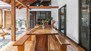 A spacious dining area with a long wooden table and benches, surrounded by large windows and potted plants. - Villa Ave del Paraiso, 7-bedroom Bed & Breakfast Villa in Playa Avellanas (Playa Avellanas)