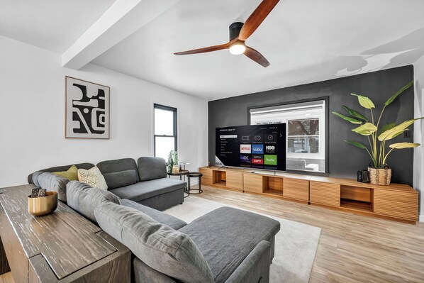 A modern living room with a sectional sofa, a wooden coffee table, a flat-screen TV, and a ceiling fan.