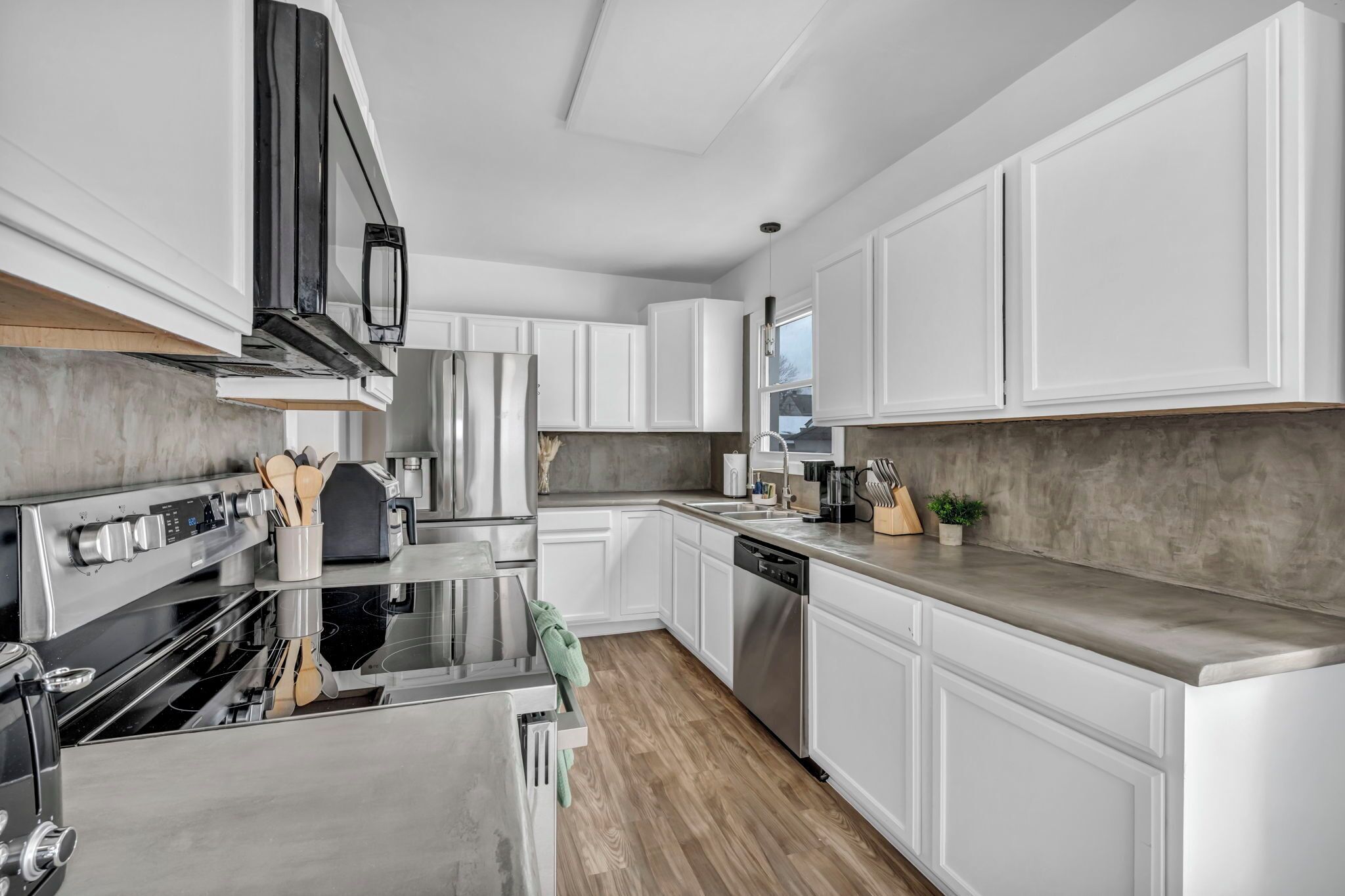 A modern kitchen with stainless steel appliances, white cabinetry, and a concrete backsplash.